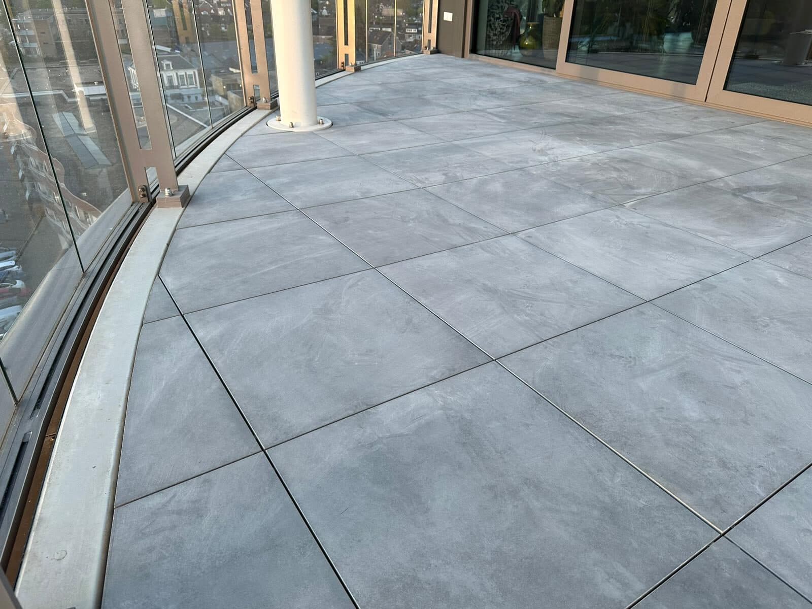 Halfrond balkon met grote grijze tegels die de ronding volgen, achter een glazen balustrade