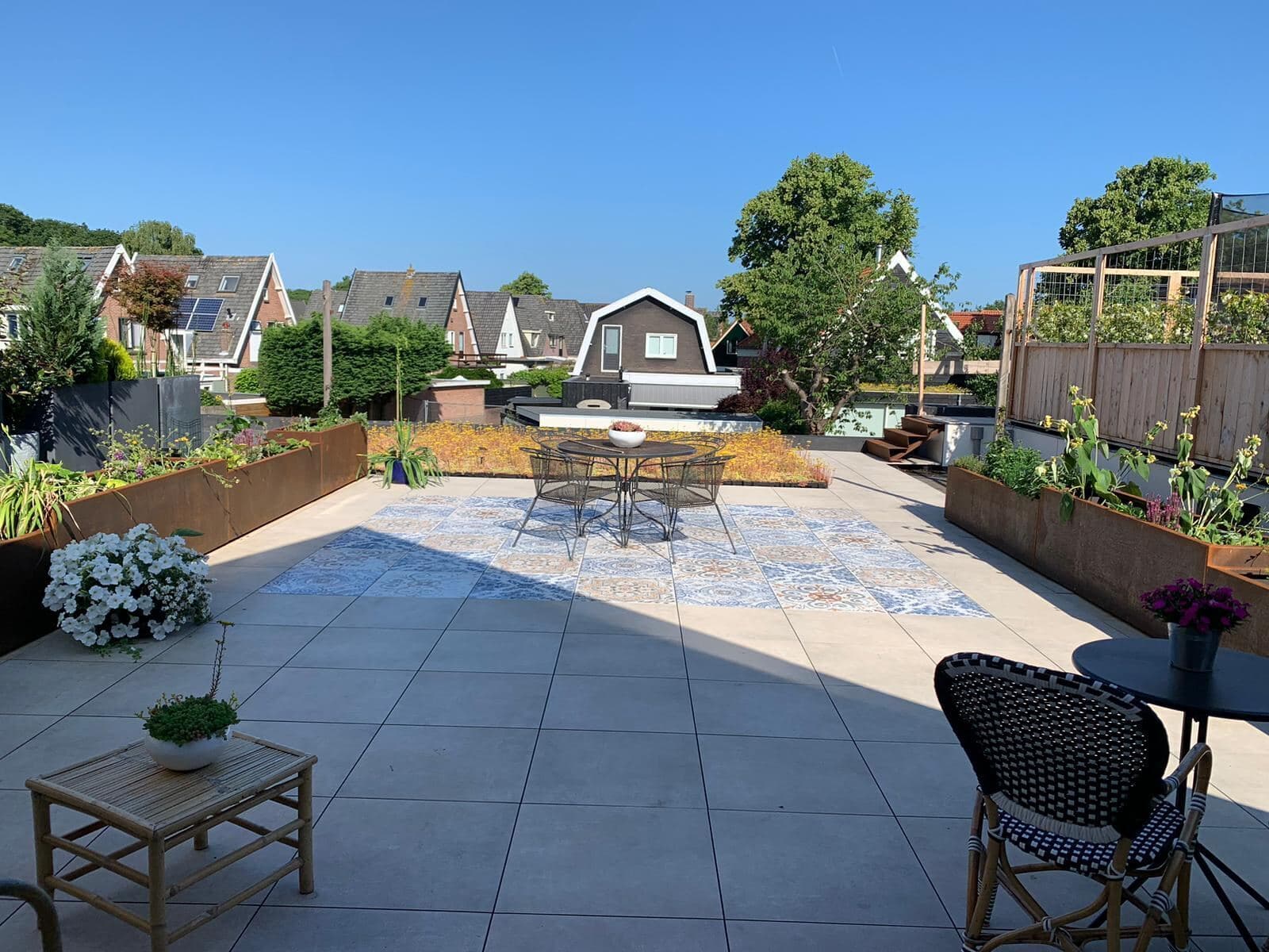Zonnig dakterras met grote grijze keramische tegels en een vlak met decortegels onder de tuintafel